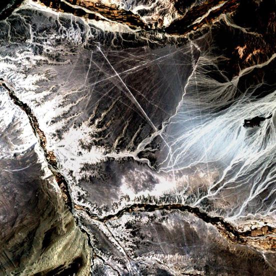 En el desierto del suroeste de Perú, entre los Andes y la costa peruana, se encuentra una meseta con enormes dibujos geométricos, espirales, figuras de animales como un mono, una araña y un hombre búho y miles de líneas perfectamente rectas. El último de estos fue dibujado hace alrededor de 1 mil años. Conocido como las líneas de Nazca, los dibujos han mistificado a científicos puesto que primero fueron descubiertos en la década de 1920. En la foto es todo lo que se aprecia de estas líneas por la banda de 15 metros pan de Landsat 7, que se ha utilizado para afilar las bandas de 30 m 3, 2 y 1.